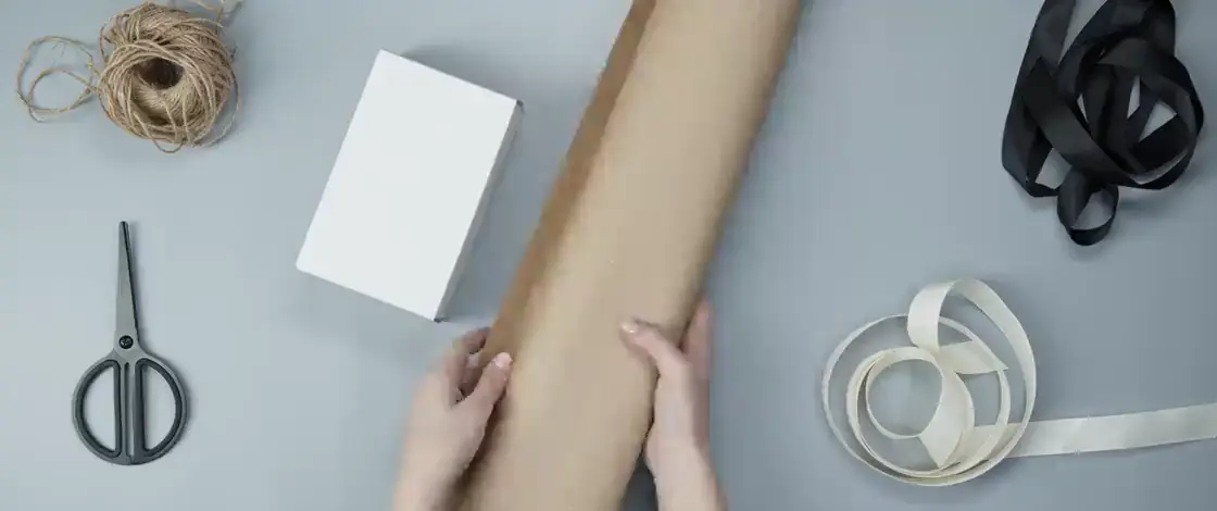 Dos manos envolviendo un paquete con papel kraft sobre una mesa